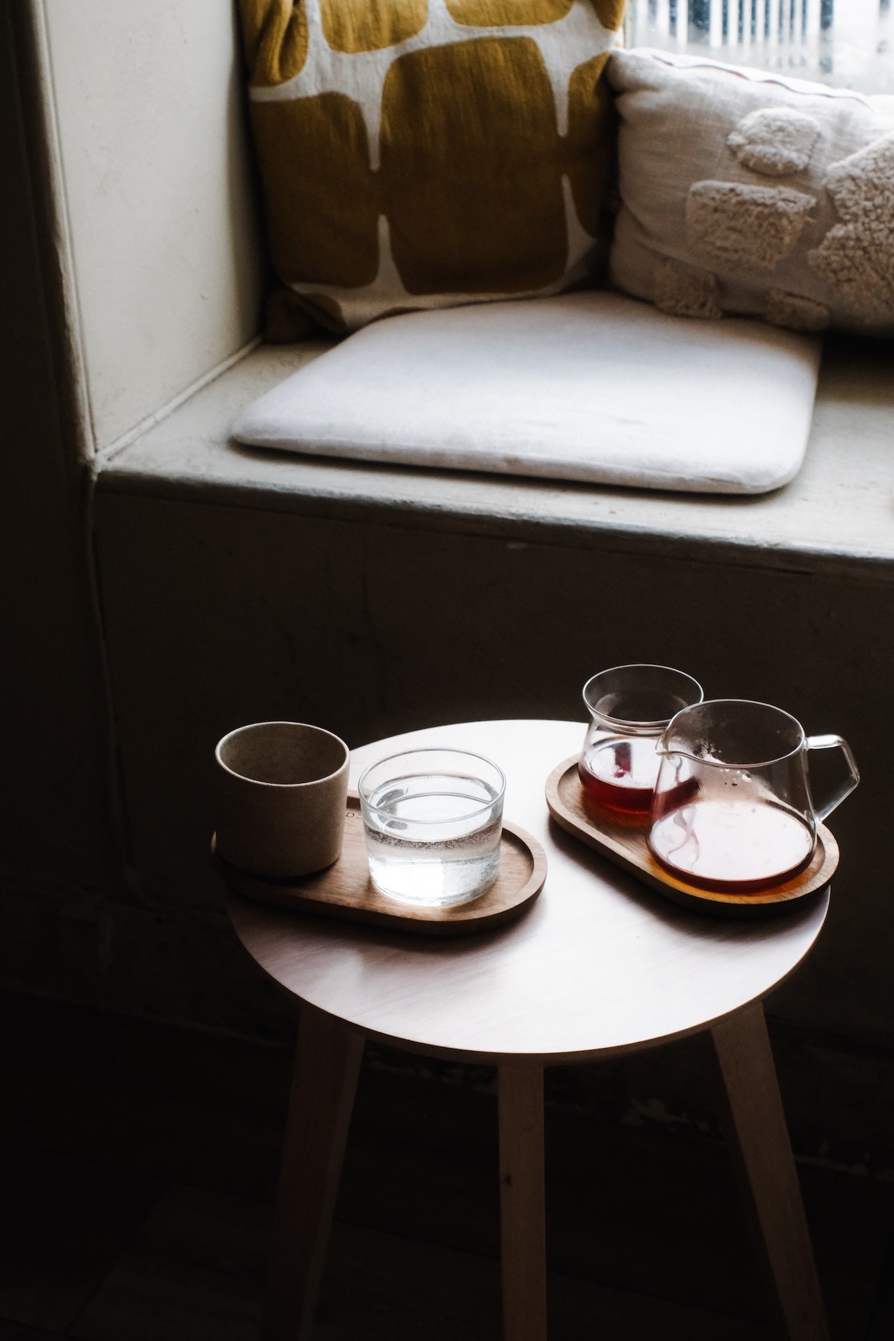 Round wooden table with tea cups and glasses on a cushioned window seat.