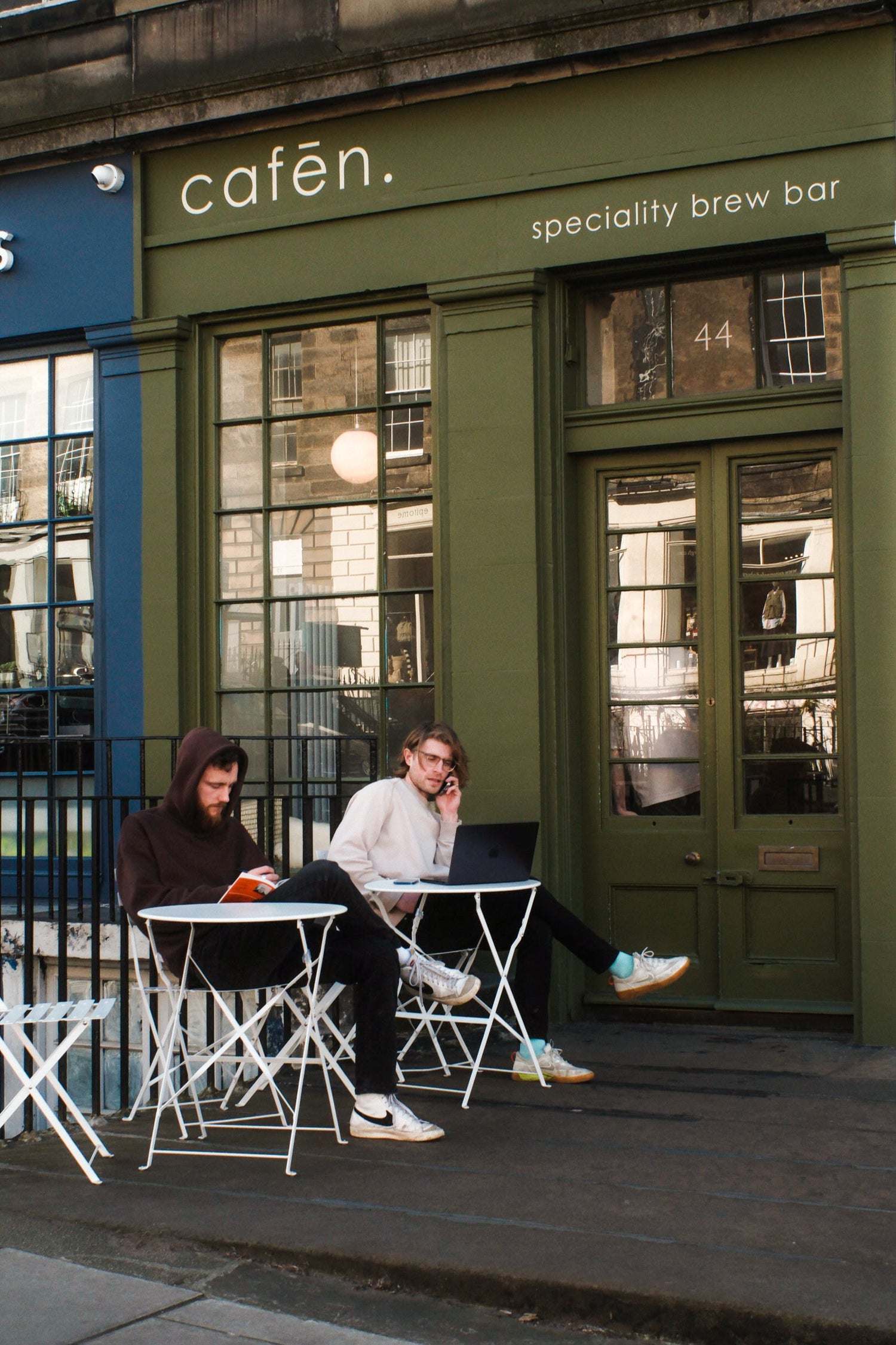 Two people sitting outside a cafe with 'cafen' sign above.