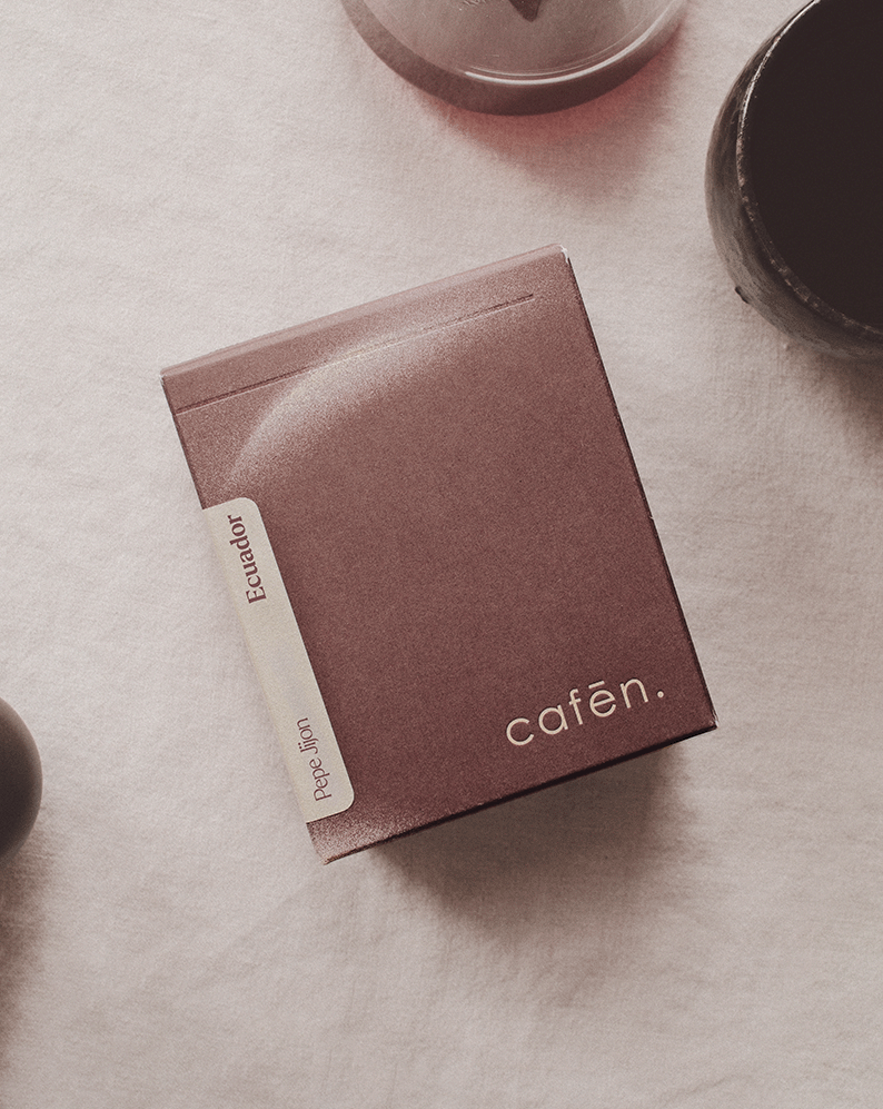 Folded pink napkin with 'cafen' branding on a beige surface with cups in the background