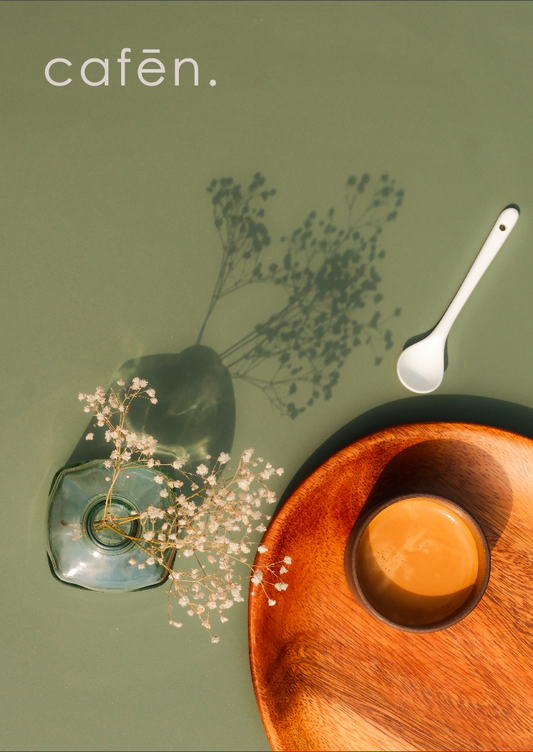 Café setting with wooden plate, cup, spoon, and flowers on a green background